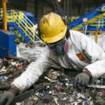 Trabajador industrial con equipo de protección clasifica materiales en una planta de procesamiento.