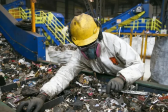 Trabajador industrial con equipo de protección clasifica materiales en una planta de procesamiento.