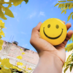Mano sostiene una cara sonriente amarilla por el Día Mundial de la Sonrisa