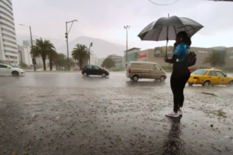 Persona con paraguas junto a una avenida de Quito durante una lluvia intensa, mientras varios vehículos circulan por la vía.